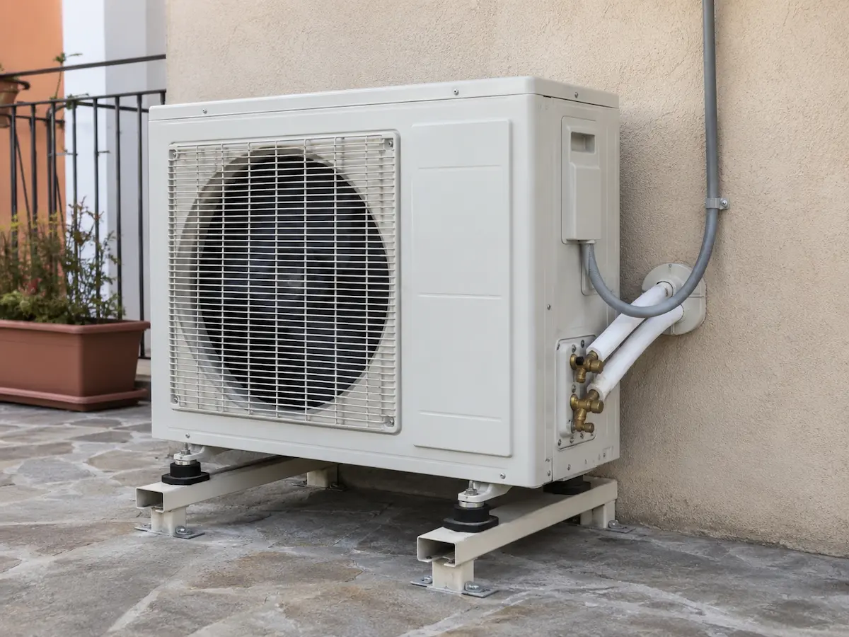 Unità esterna di pompa di calore installata su supporti antivibranti con tubazioni e raccordi alla struttura dell’edificio